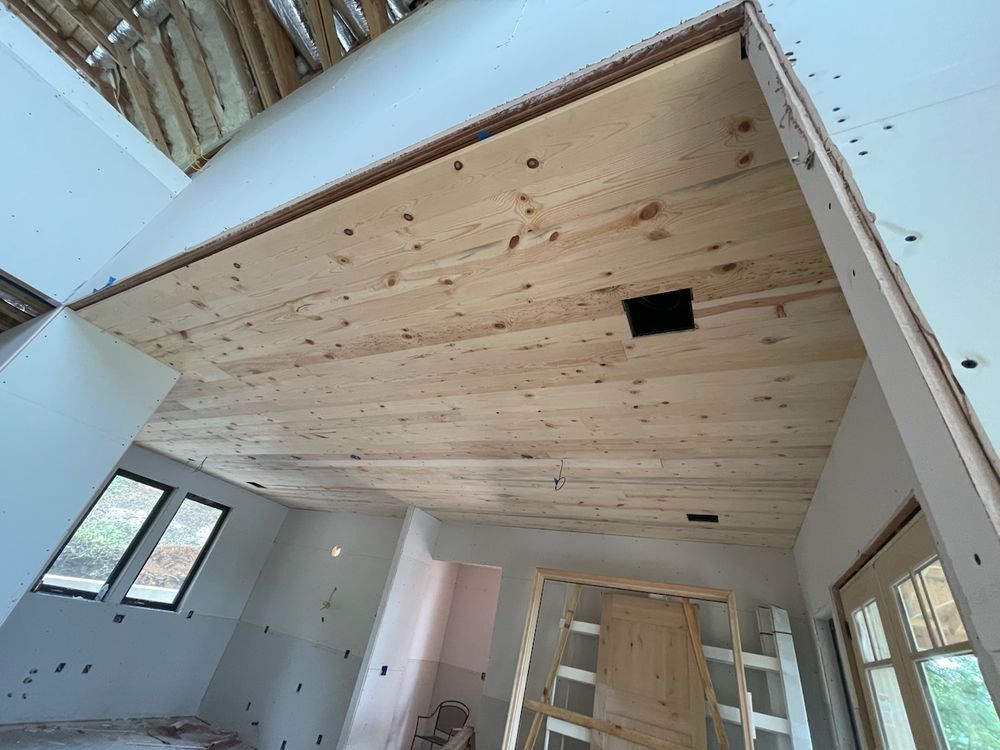 Interior view of a room under construction with a wooden ceiling and walls, drywall and unfinished doorways.
