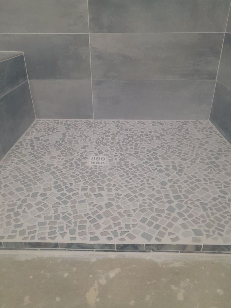 Shower with blue-gray tile walls and mosaic tile floor. A small curb borders the shower.