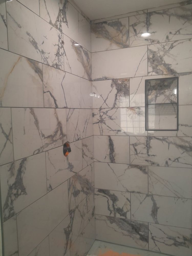 Shower with white marble-patterned tiles, built-in shelf, and unfinished plumbing.