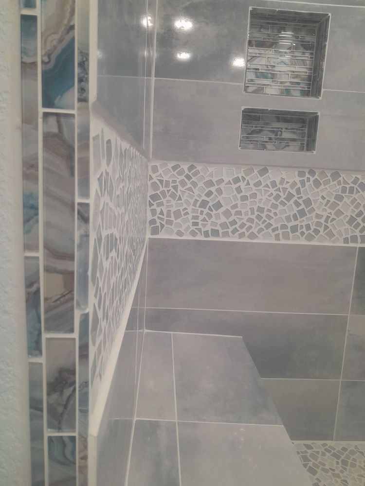 Blue-tiled shower interior with decorative mosaic tile accents, gray walls, and built-in storage.
