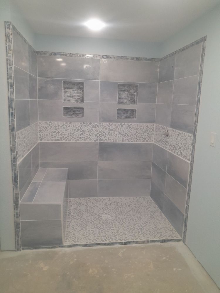 Gray tiled shower with a bench, two niches, and pebble floor.