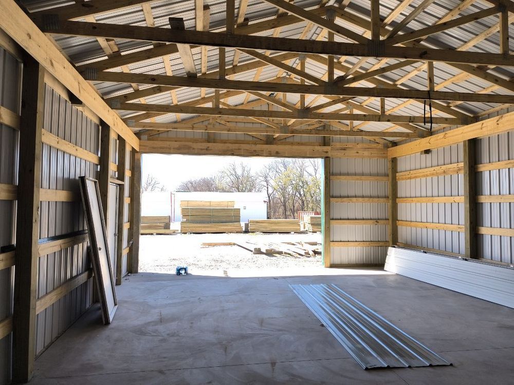 Interior of a new metal building with concrete floor, open doorway, and wooden beams.