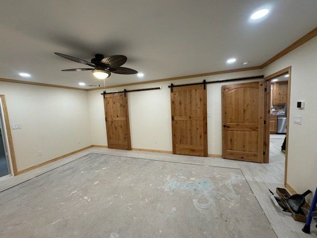 A room with three wooden barn doors, tan walls, and a ceiling fan. The floor is bare concrete.
