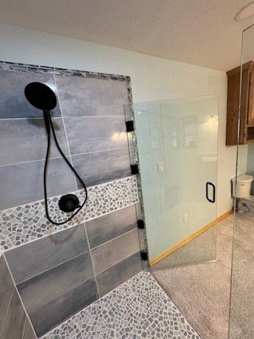 Modern shower with black fixtures, glass door, gray tiles, and a pebble floor.