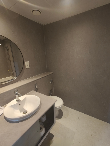 Small gray bathroom with a white sink, round mirror, toilet, and textured wall.