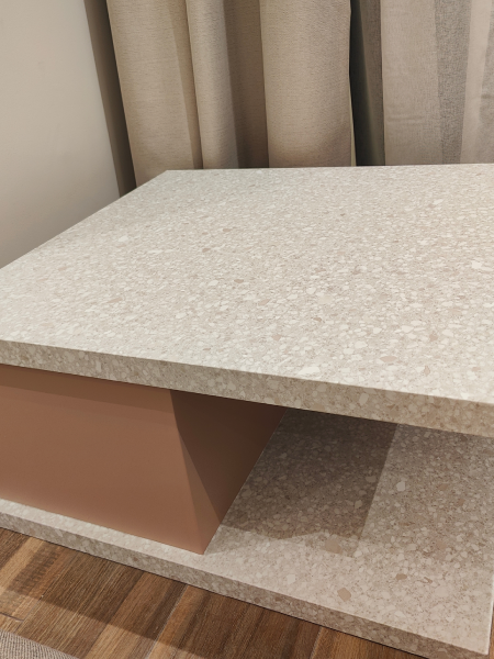 Speckled beige shelf with a pink side panel beside beige curtains and a wood floor