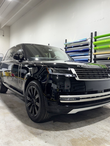 Black luxury SUV in a garage, front three-quarter view, with black wheels and wall-mounted racks in the background