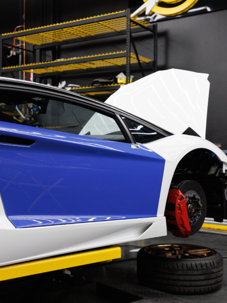 Blue sports car with white front end lifted in a garage, hood open and red brake visible