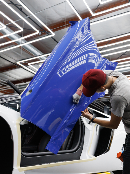 Worker installing a blue car door panel in an auto shop