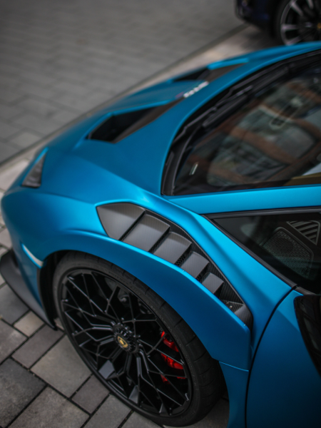 Blue sports car close-up with black wheel and carbon-fiber trim on a paved surface