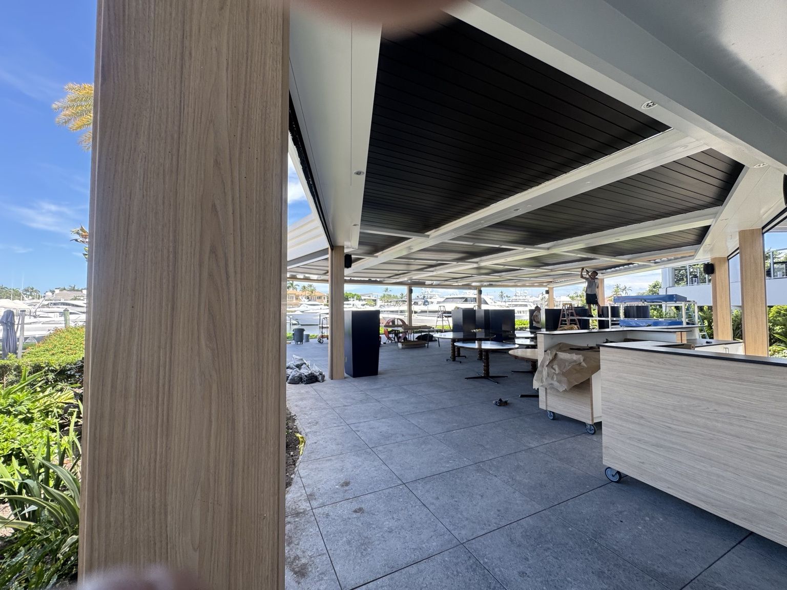 Outdoor patio seating area with white counters, wood columns, and a covered roof under a blue sky.
