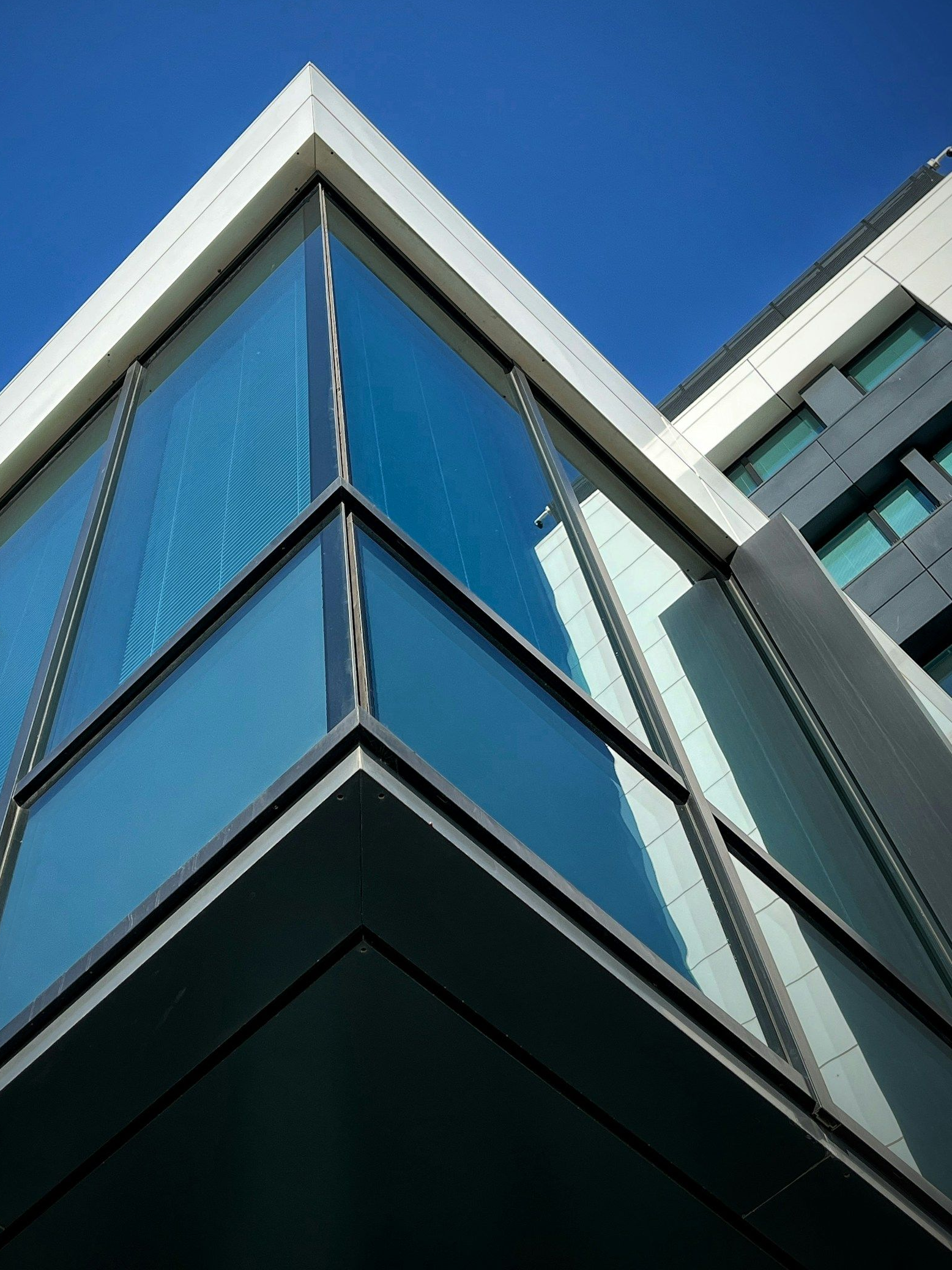 Low-angle view of a modern building corner with blue glass panels and white trim against a blue sky