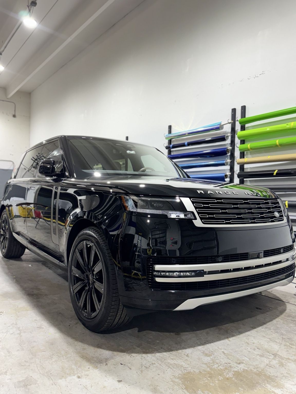 Gloved hand polishing a glossy black car surface with a yellow cloth