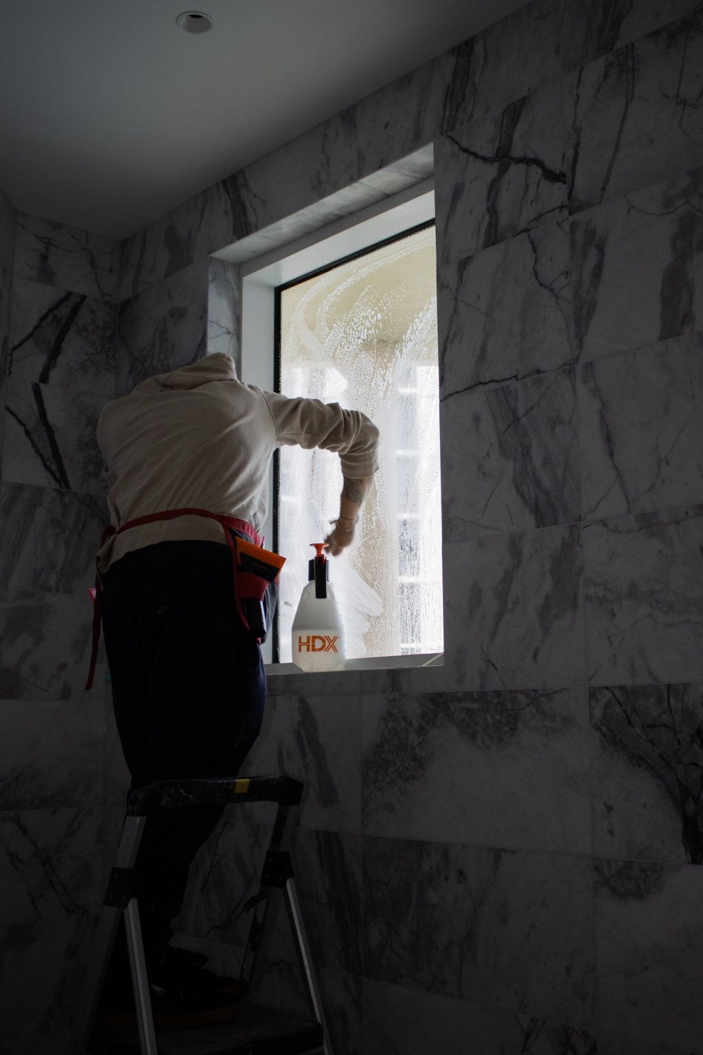 Person painting a small window frame in a room with gray marble-patterned walls and a ladder.