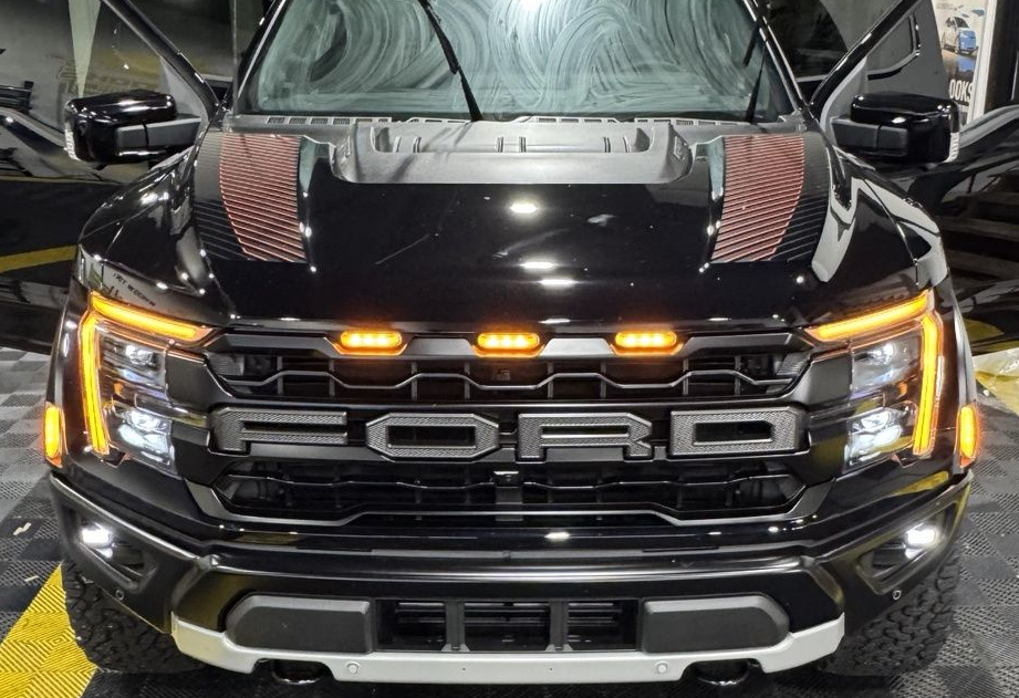 Black pickup truck with orange lights in a garage, viewed from the front, doors open