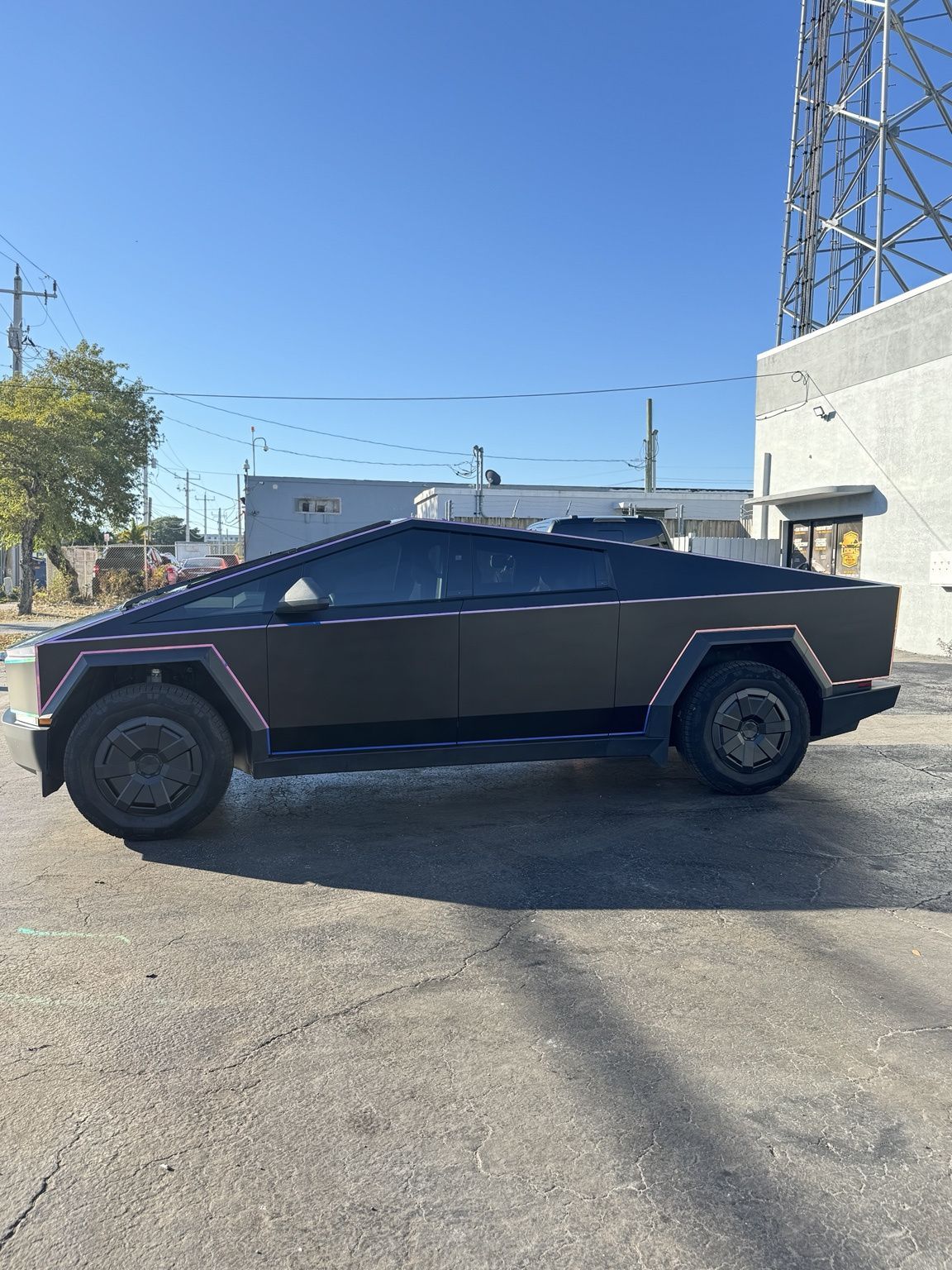 Matte black Cybertruck parked in an industrial lot under a clear blue sky.