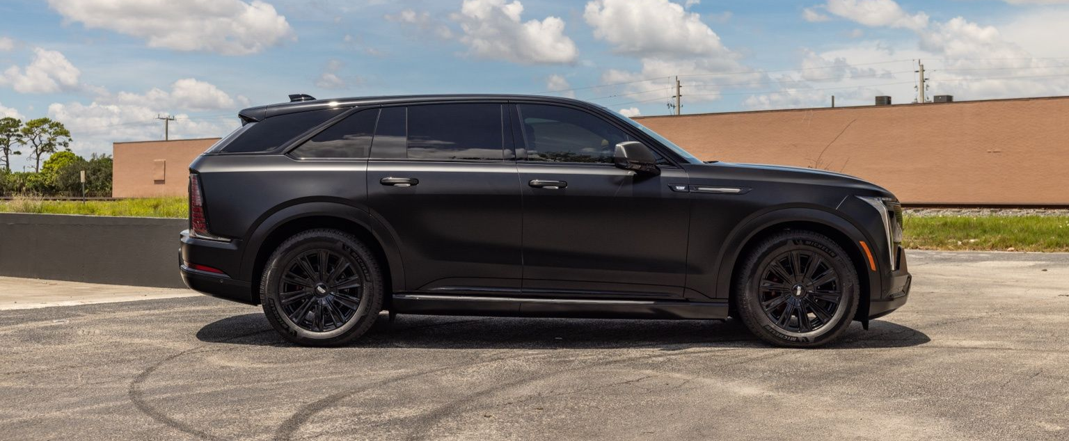 Black SUV parked in a lot under a partly cloudy sky with a tan wall in the background