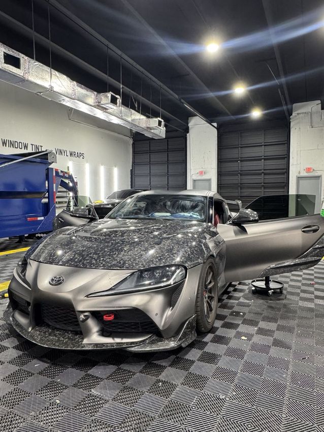 Matte gray sports car in a showroom with a person opening the door
