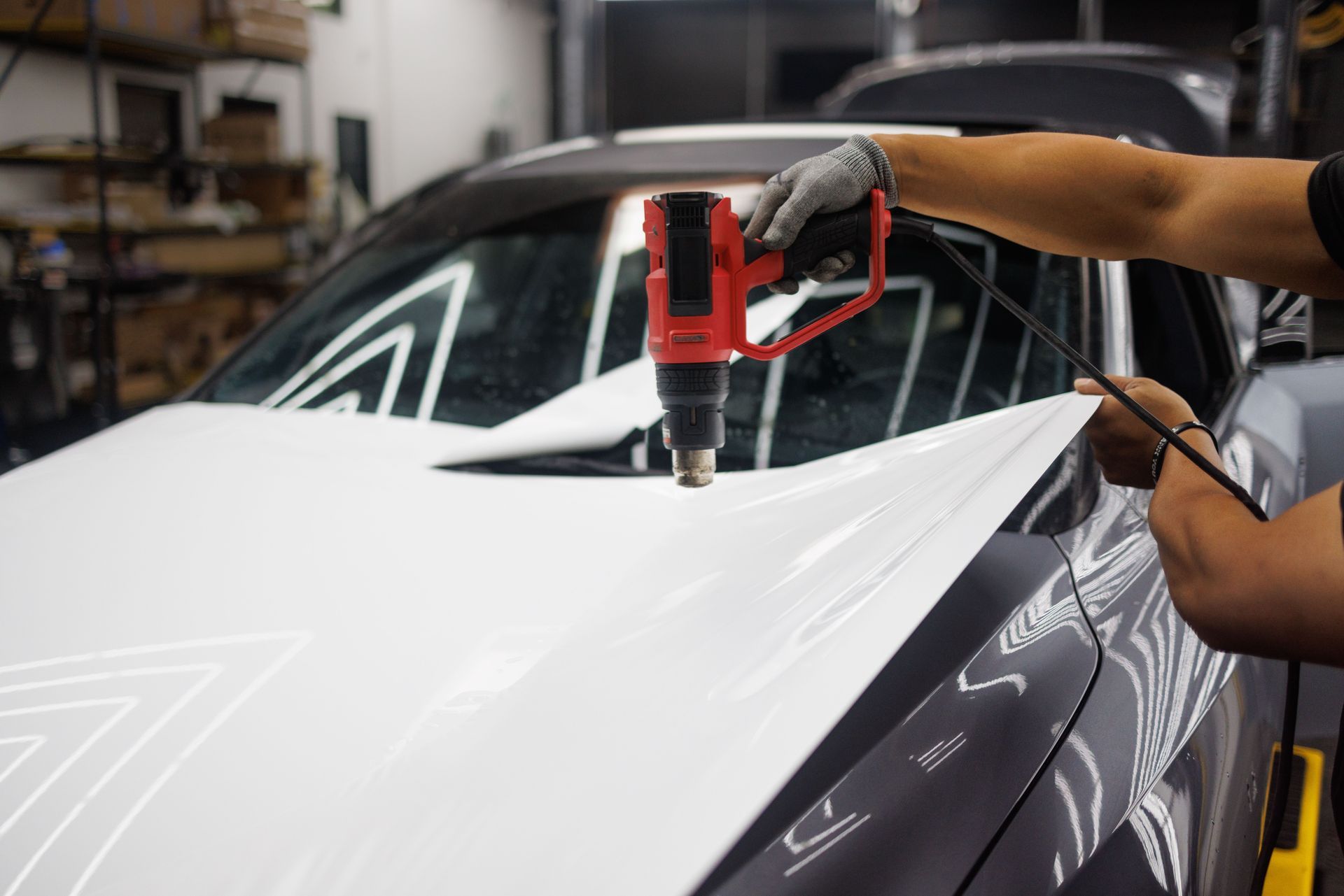 Car wrapped in white vinyl as a technician uses a heat gun on the hood in a garage