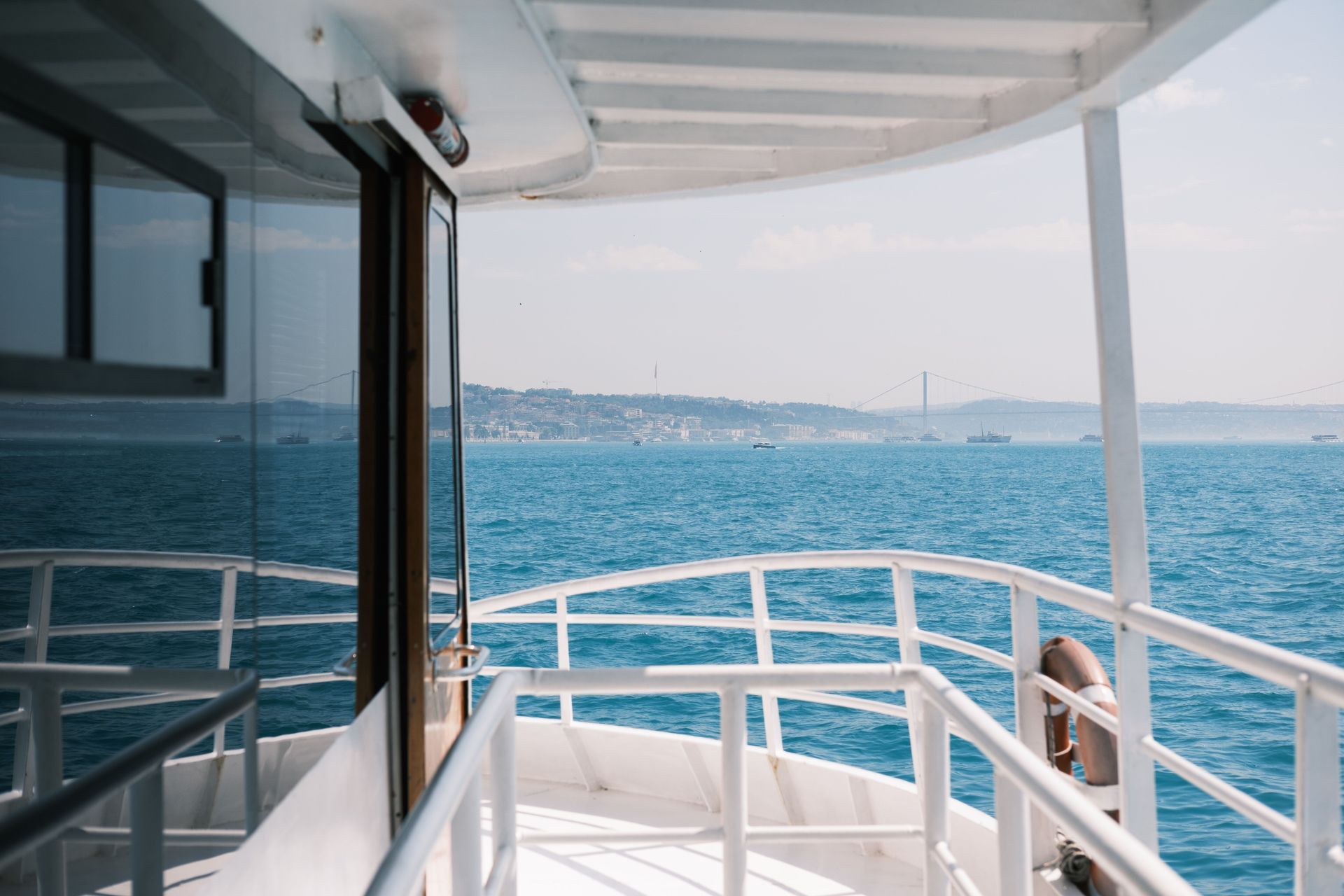 View from a boat deck with white railings overlooking blue water and a distant coastline