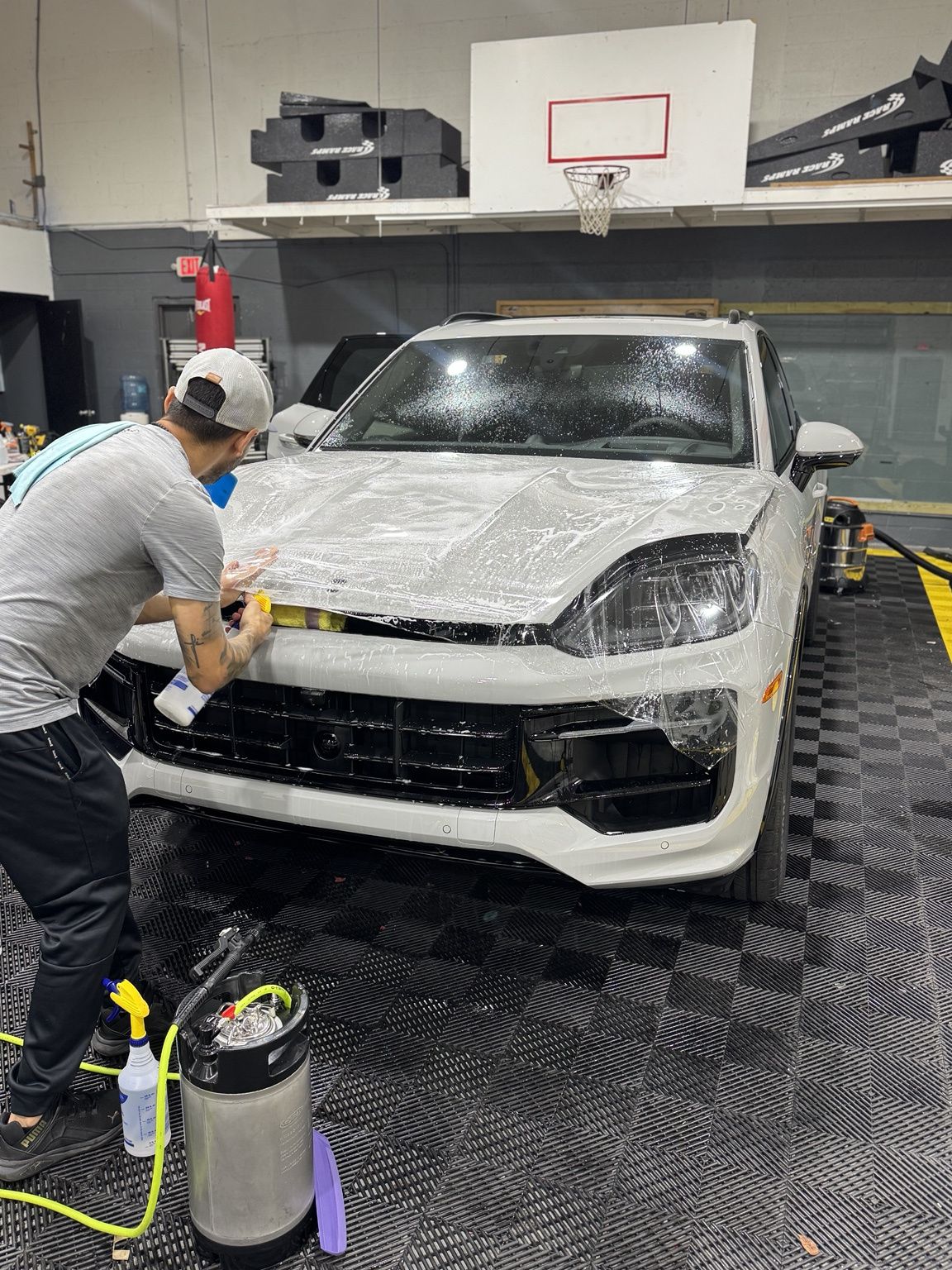Detailing shop worker washing a white SUV with a foam sprayer in a garage