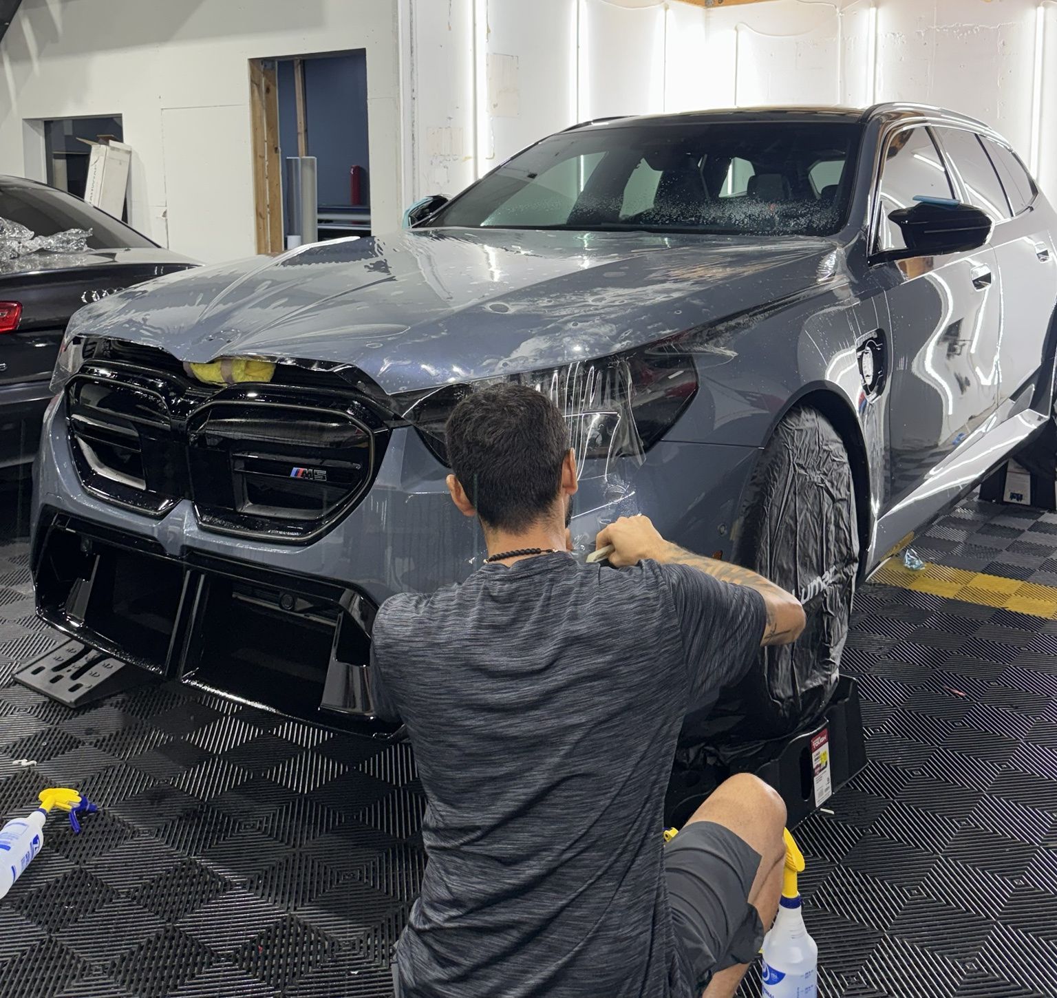 Detailing worker cleaning a gray SUV in a bright indoor auto shop