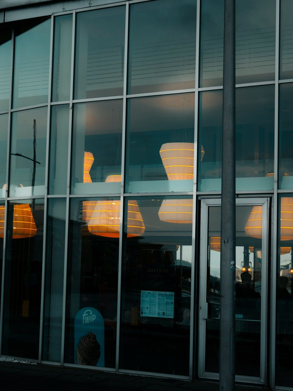 Glass-front building entrance with tall windows and warm interior lights reflected on the facade