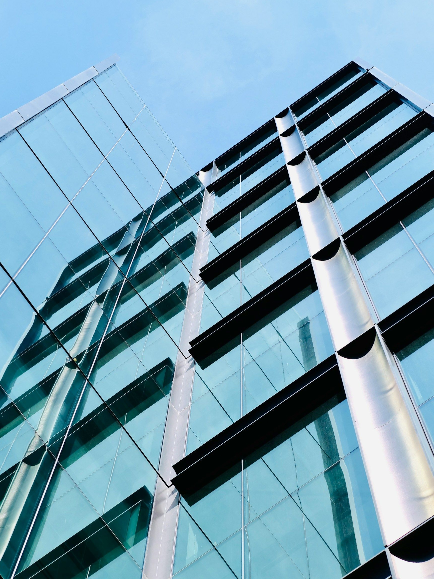 Modern glass office building viewed from below against a blue sky