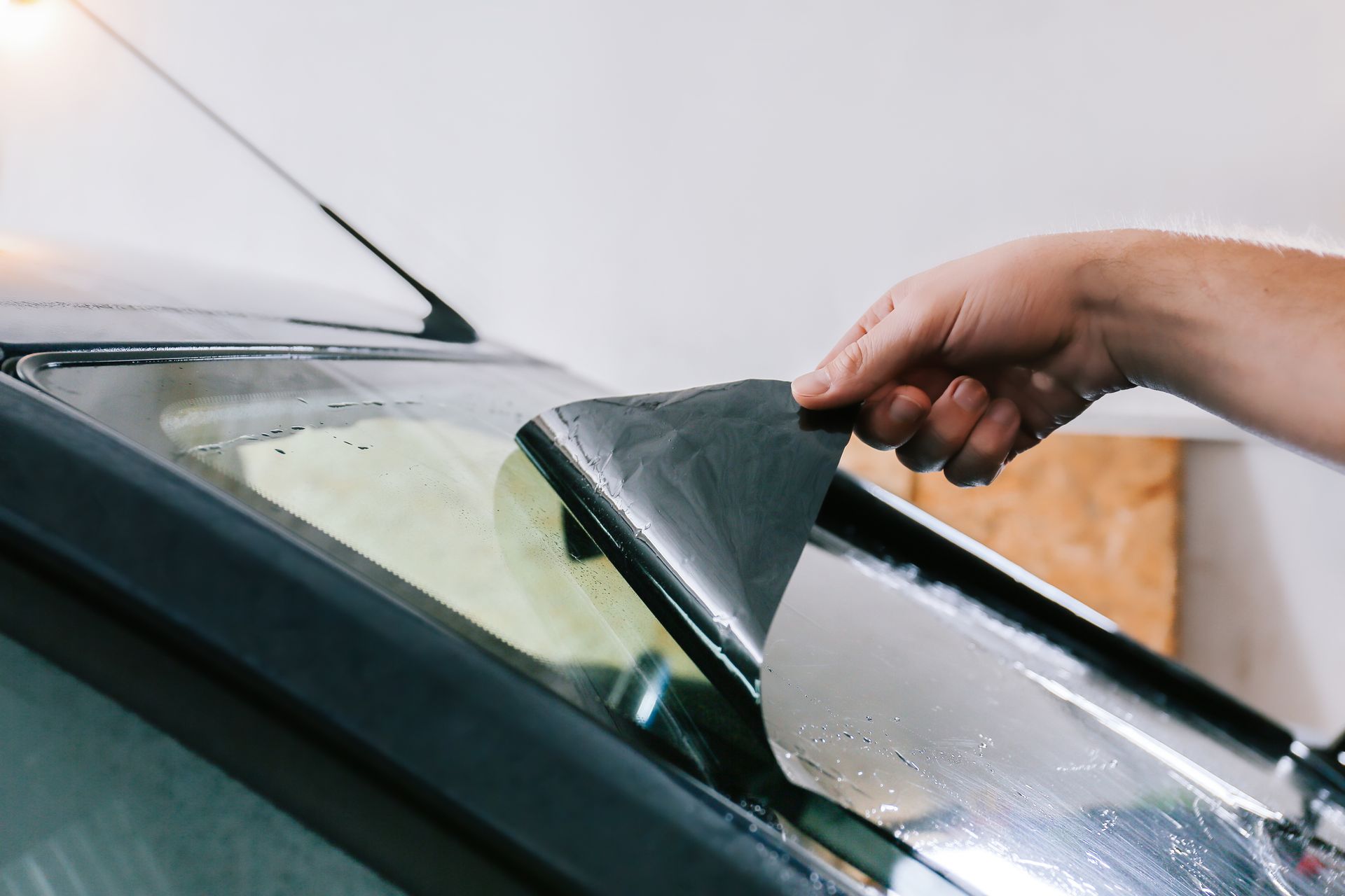 Hand scraping a car windshield with a black squeegee to remove water and dirt