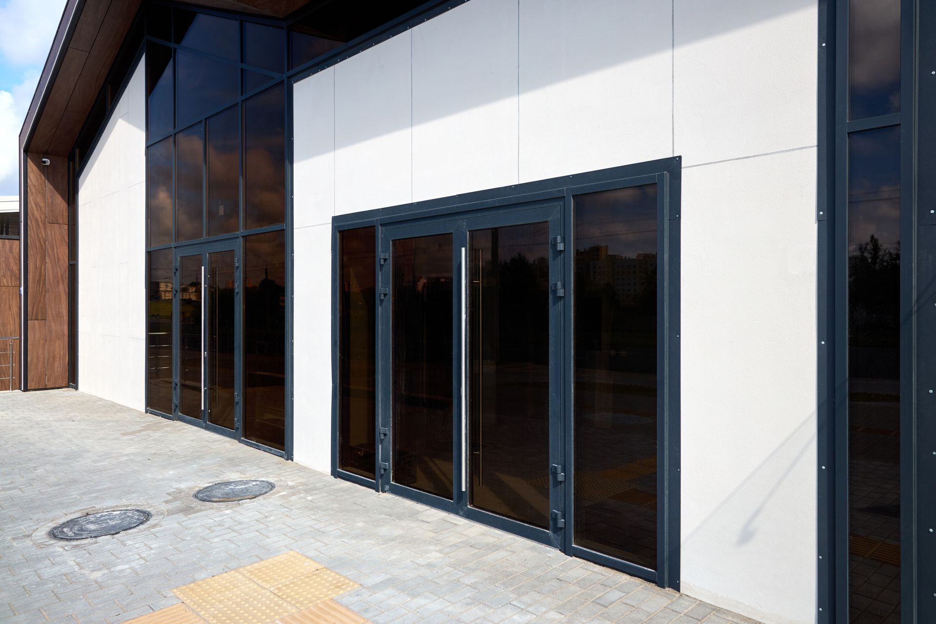 Modern building facade with glass double doors and large windows on a paved entrance.
