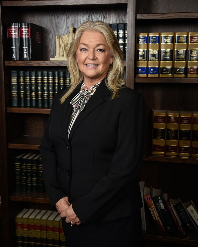 A woman in a black suit is standing in front of a bookshelf filled with books.