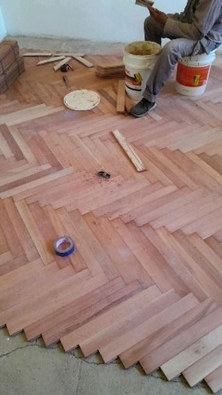 Instalación de piso de madera en curso con patrón de espiga, herramientas, cubos de adhesivo y un trabajador