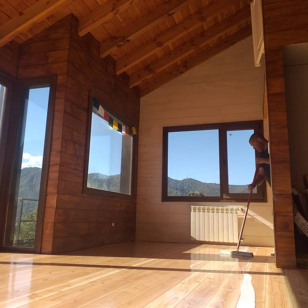 Habitación vacía de madera con techo inclinado, grandes ventanales y un radiador