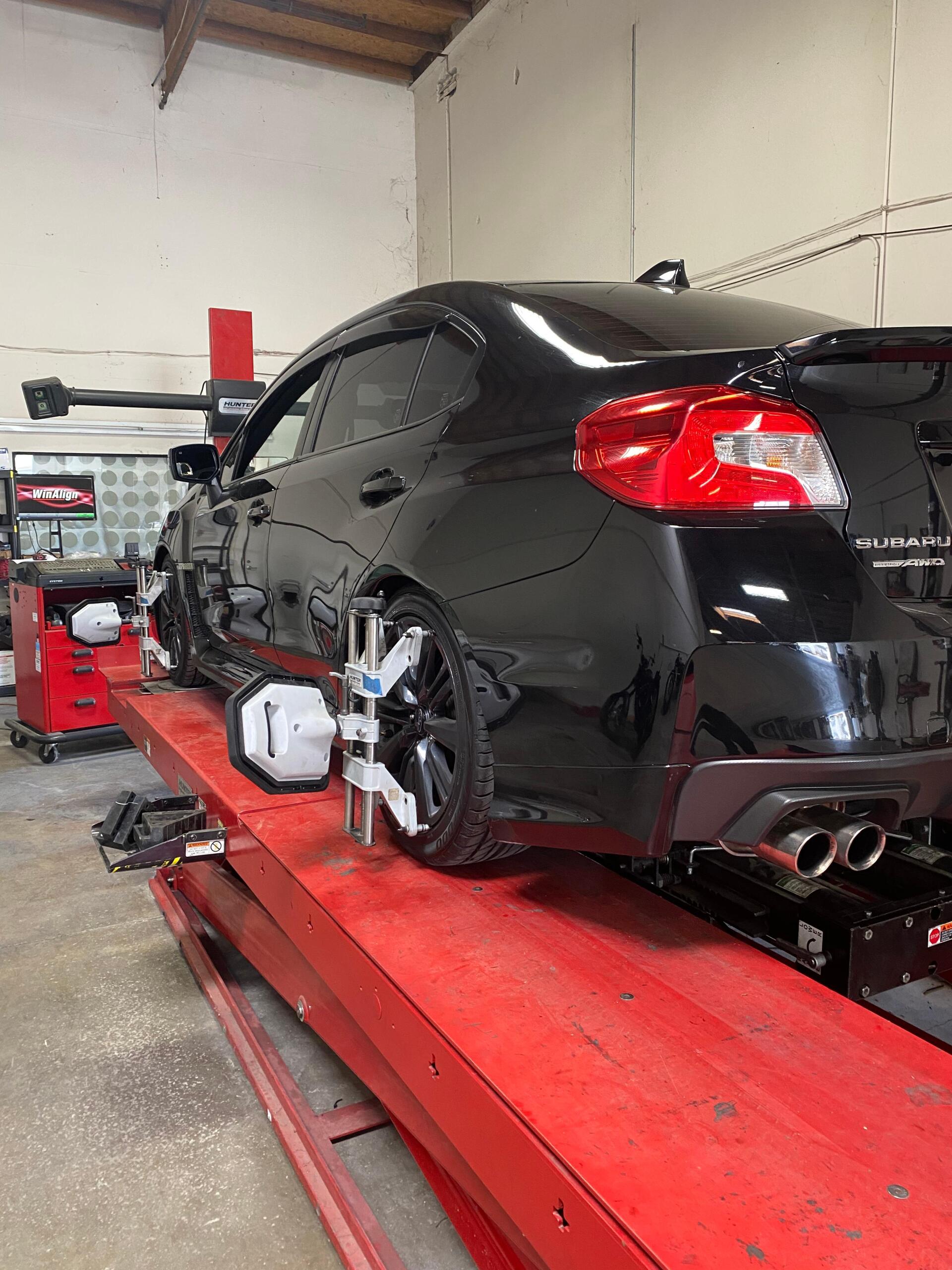A black car on a lift undergoing wheel alignment | JCR Performance, Your Tire Repair expert in Sacramento, CA