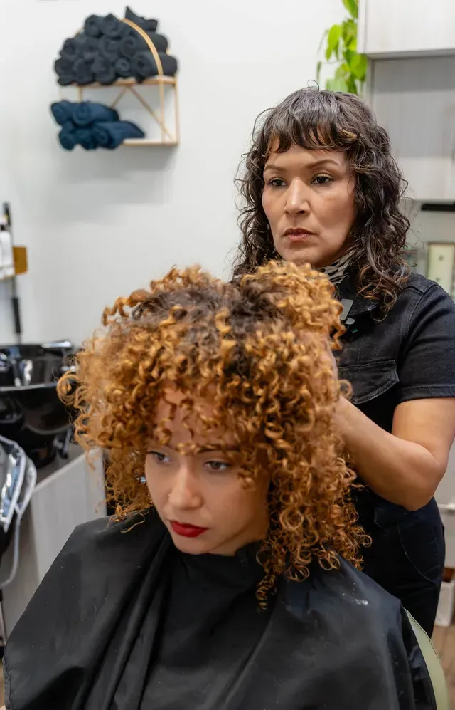 Stylist adjusting curly hair on seated client in a salon chair