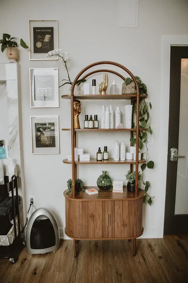 Wooden shelving unit with plants and bottles in a minimalist room, beside a black door and wooden floor