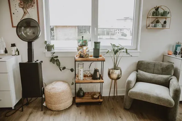 Cozy living room with neutral chair, wooden shelf, plants, round mirror, and soft daylight through a window