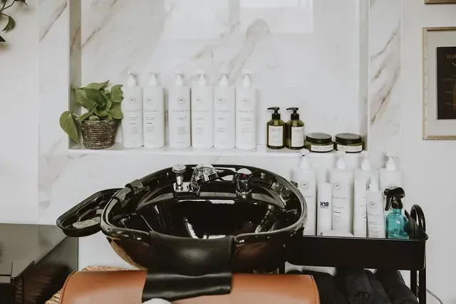 Black salon shampoo bowl with shelves of hair products in a bright white interior