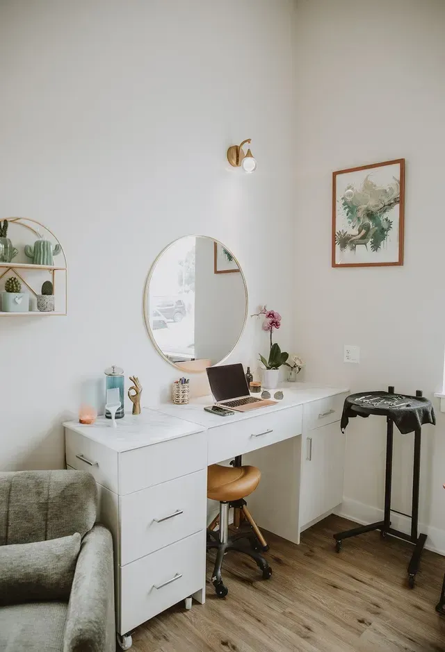 White vanity desk with oval mirror, stool, decor, and a clothing rack in a bright bedroom corner.