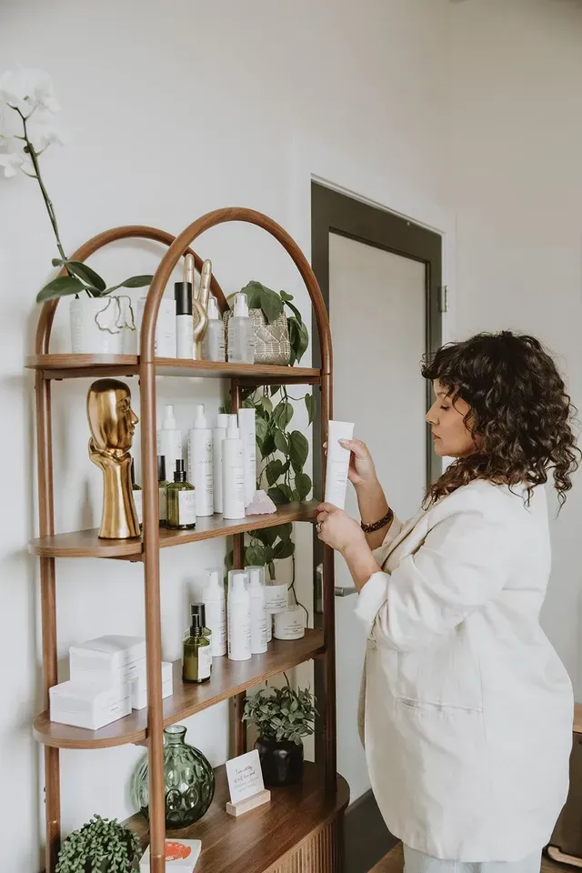 Person in white coat inspecting products on a wooden shelf in a bright room