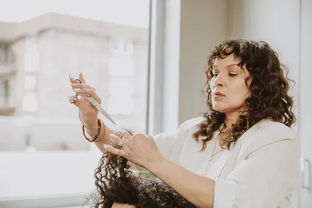 Woman with curly hair styling another person’s hair in a bright salon setting