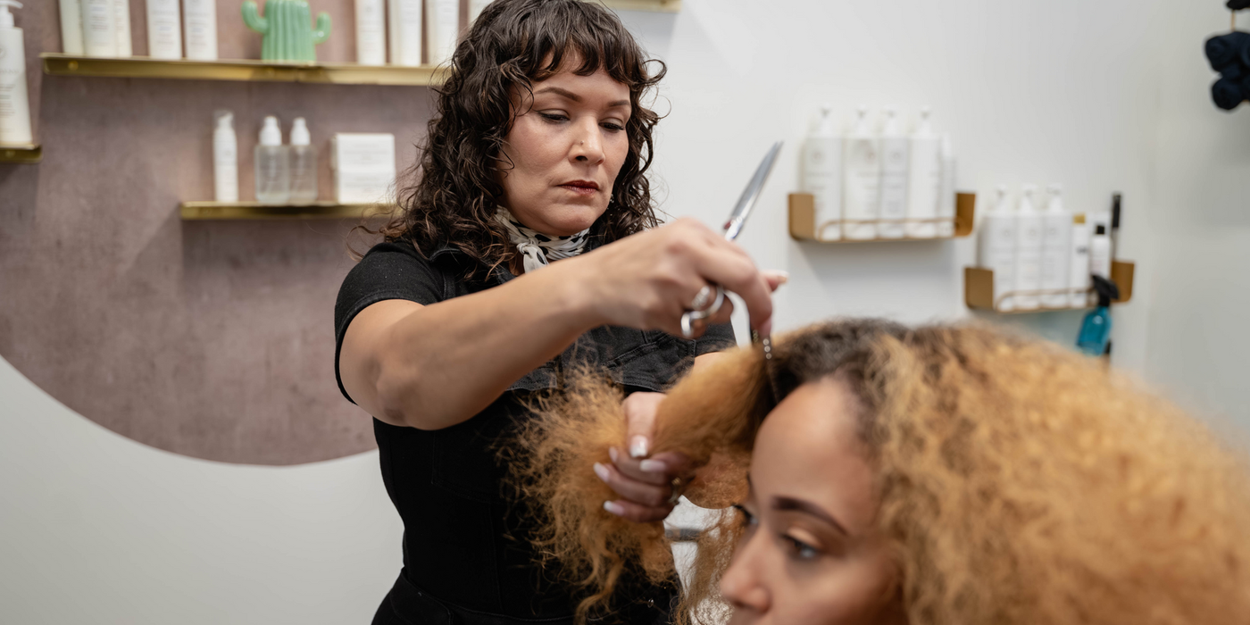 Stylist cutting a client’s curly hair in a salon with product shelves in the background