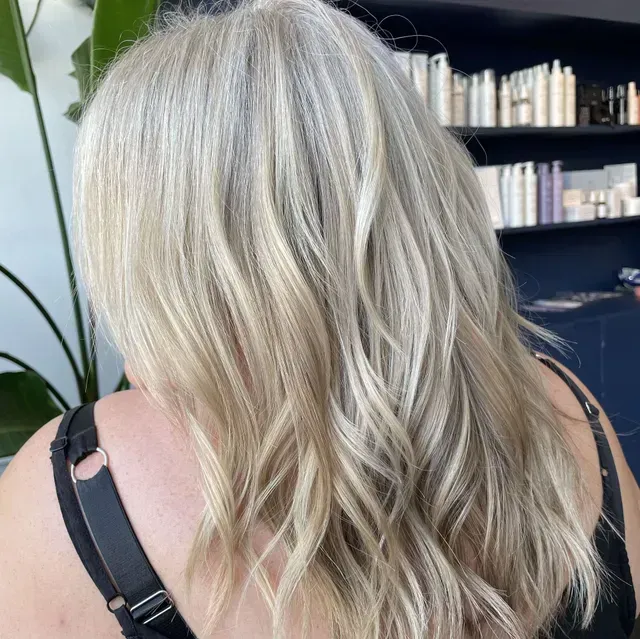 Long wavy platinum blonde hair from behind, with a black strap on the shoulder.