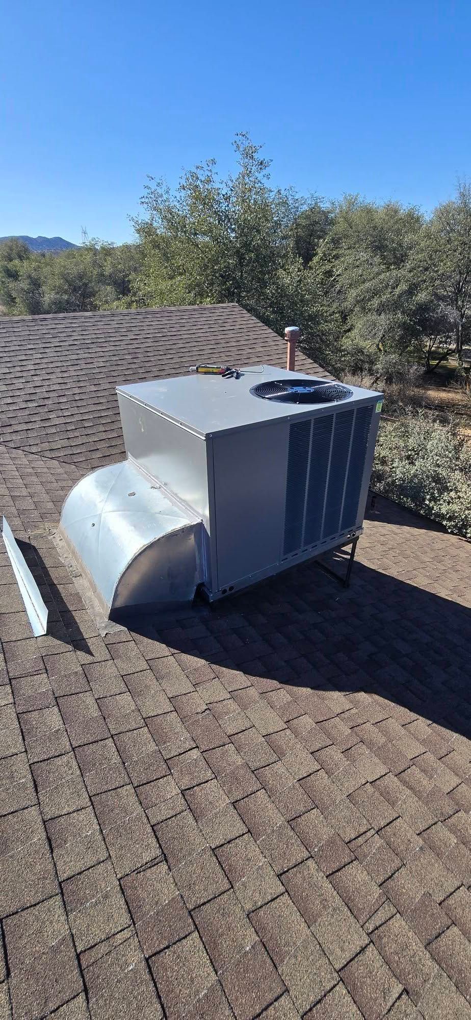 White HVAC unit on a shingled roof with desert trees in the background