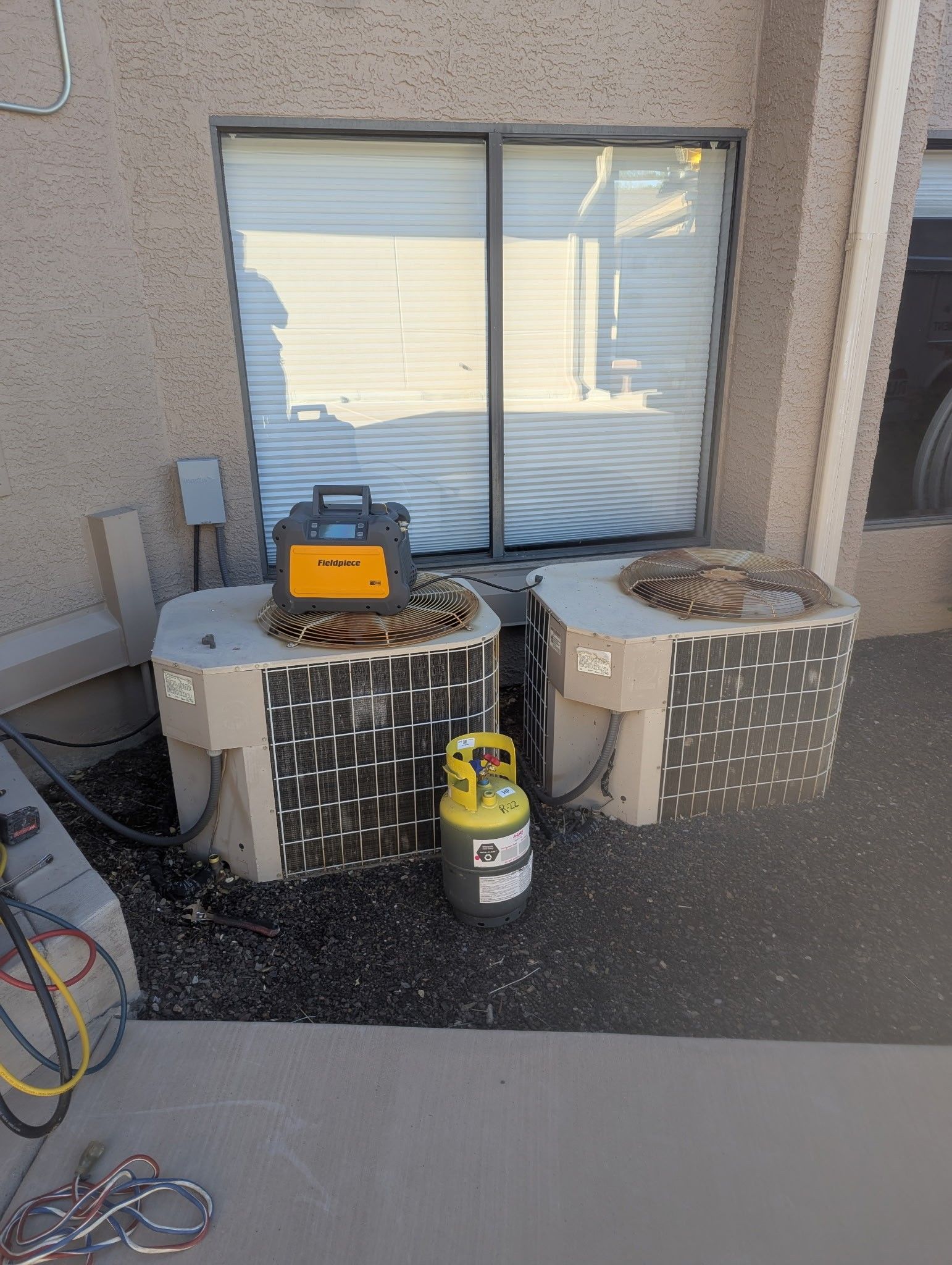 HVAC units with a yellow tank and a diagnostic tool outside a building, next to a window with blinds.