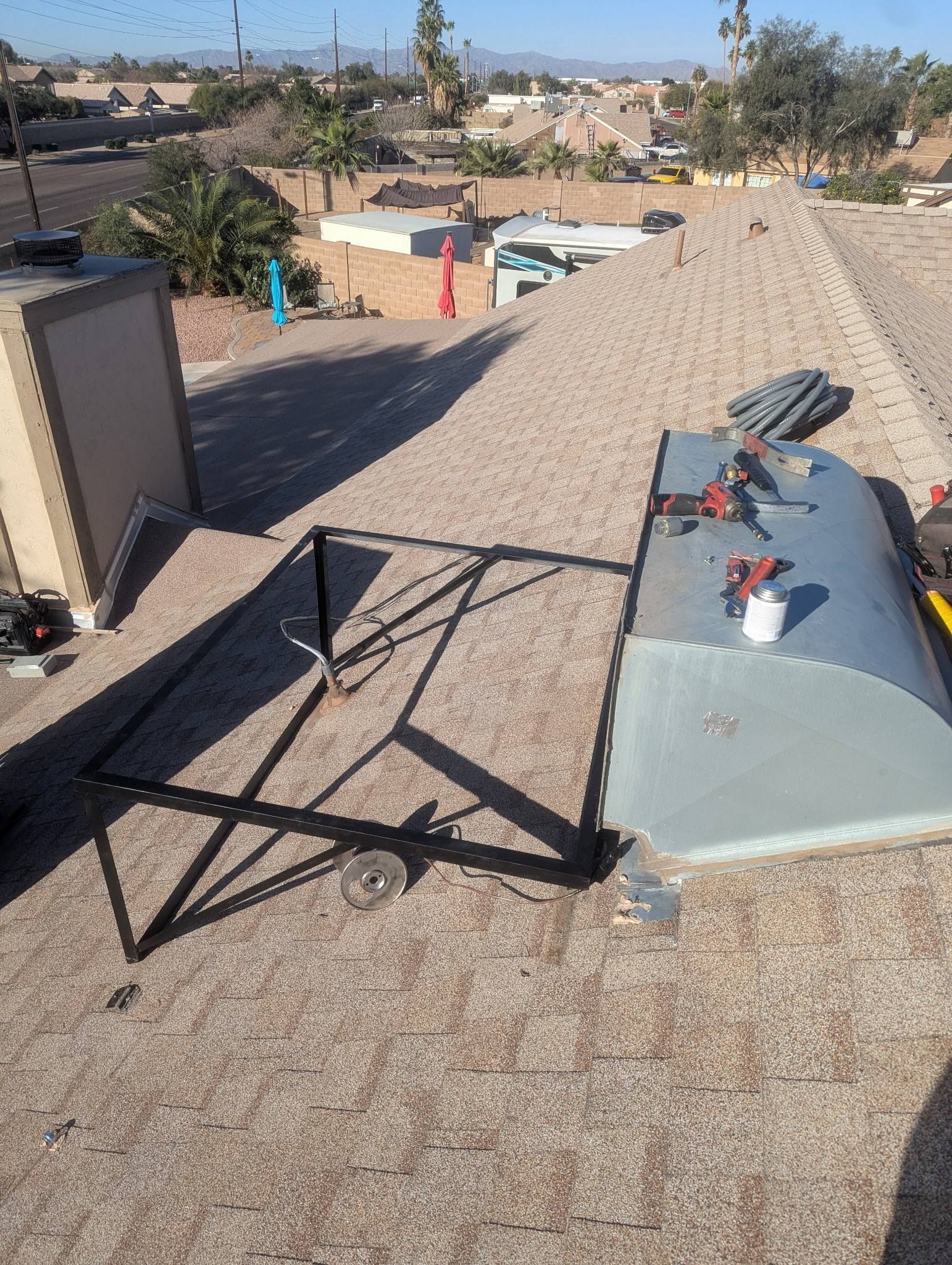 Rooftop HVAC unit beside a metal chair on a gravel roof, with nearby houses and trees in the distance