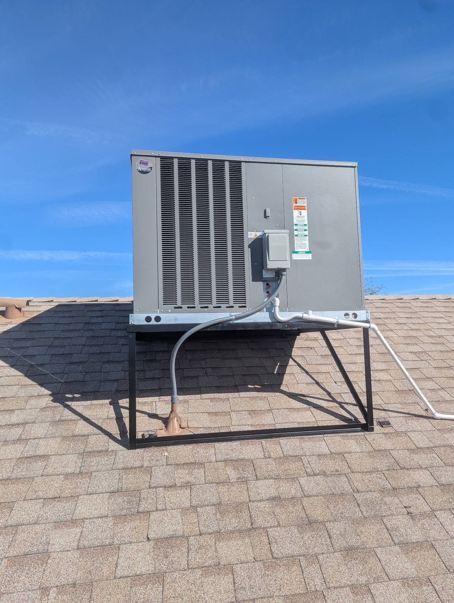 Gray rooftop HVAC unit on metal stand against a blue sky on a shingled roof
