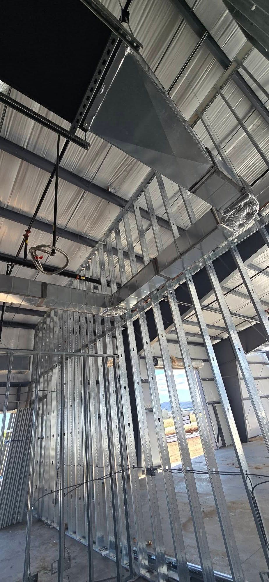 Exposed metal framing and beams inside a building under construction, with a steel staircase overhead