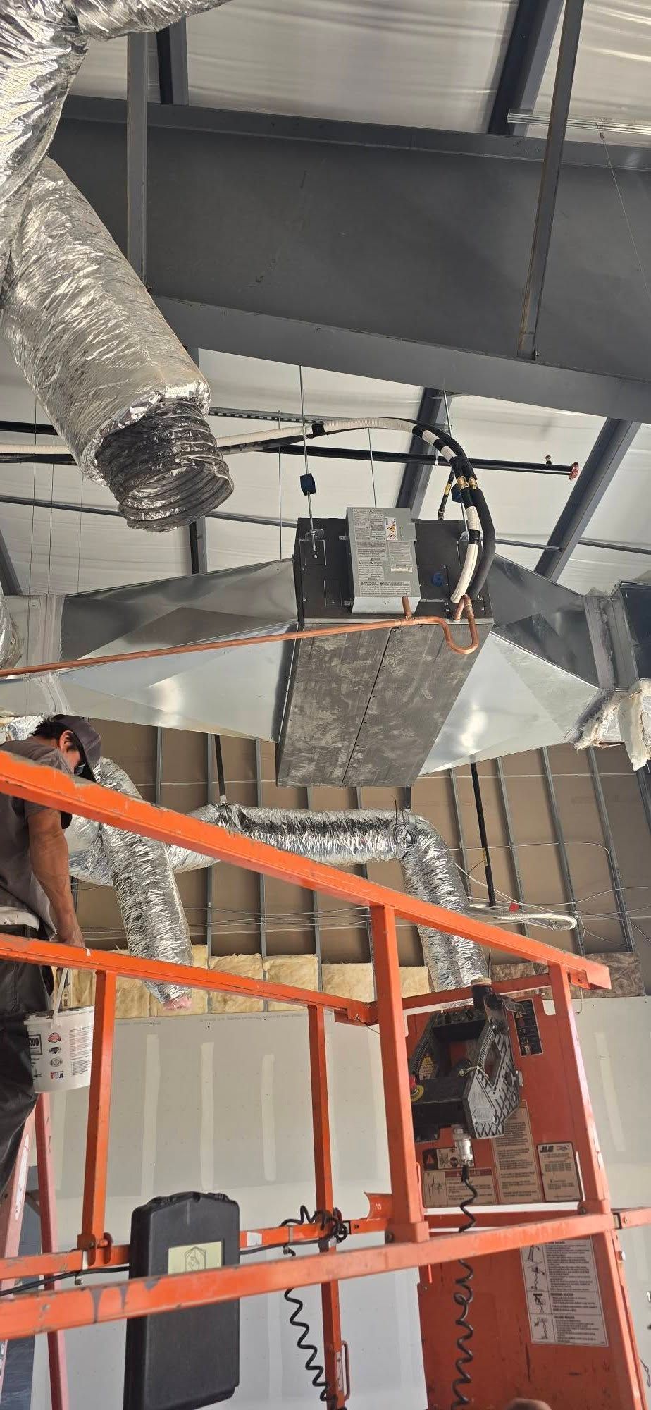 Industrial ceiling with exposed ducts and orange scaffolding in a construction area