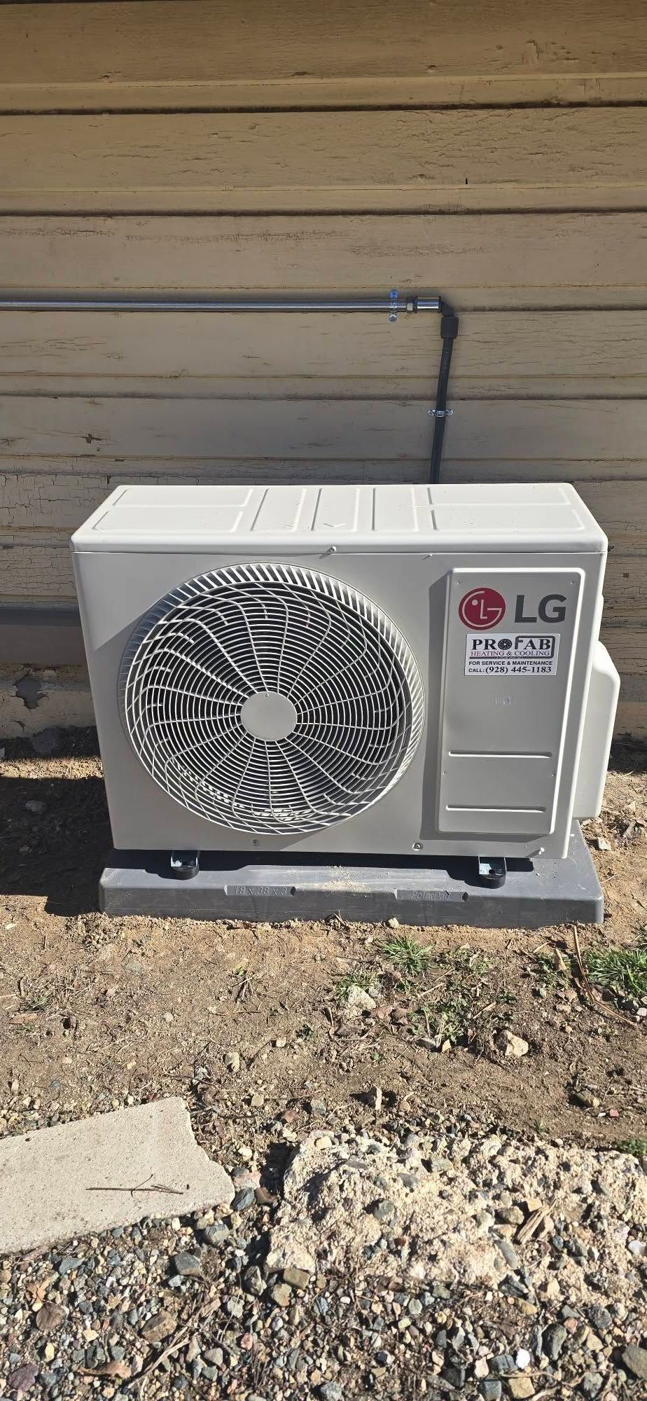 Outdoor LG air conditioner unit beside a beige house wall on a gravel bed.